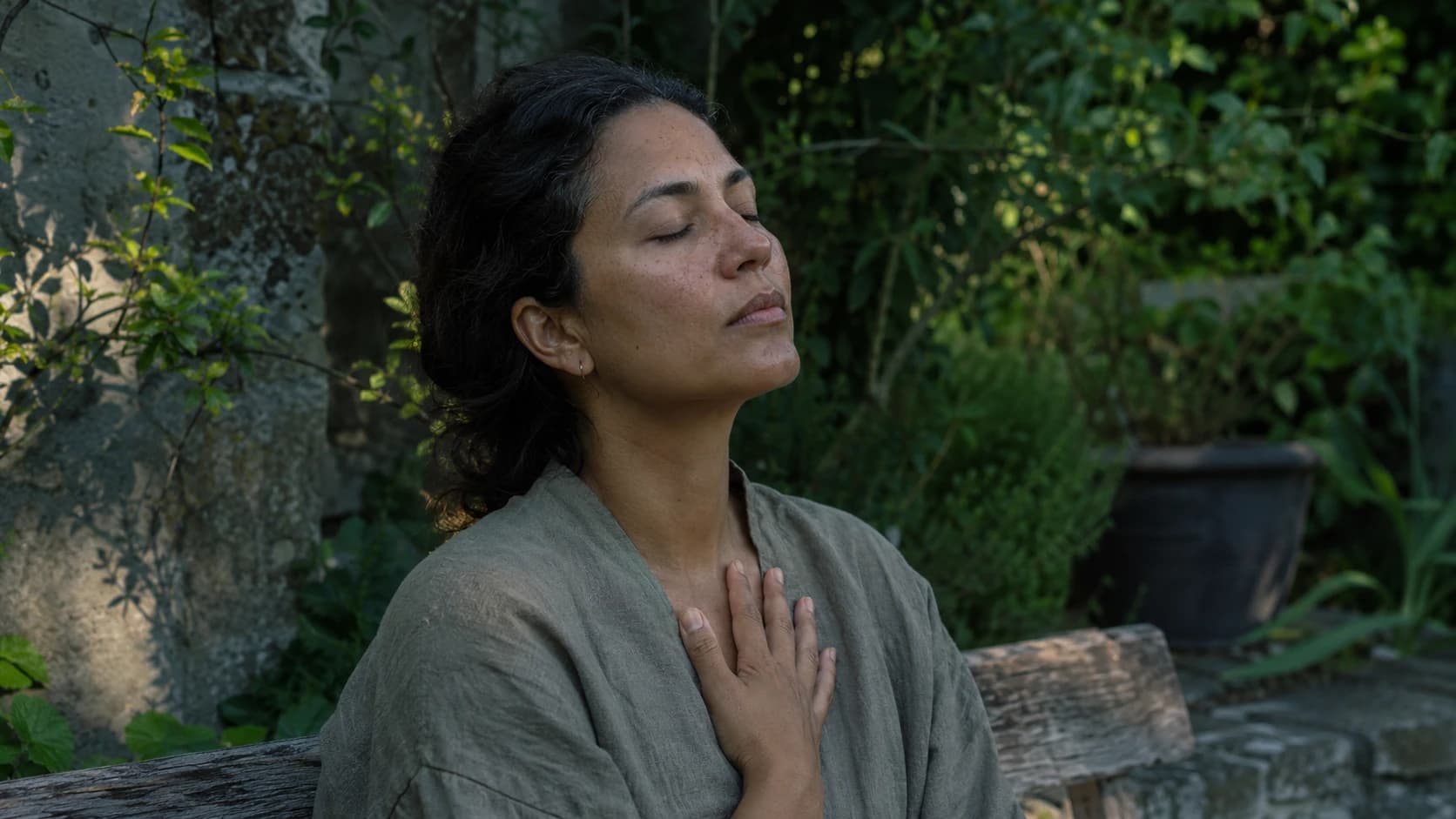Woman seated in a garden with a hand on the chest, practicing slow breathing to calm the nervous system